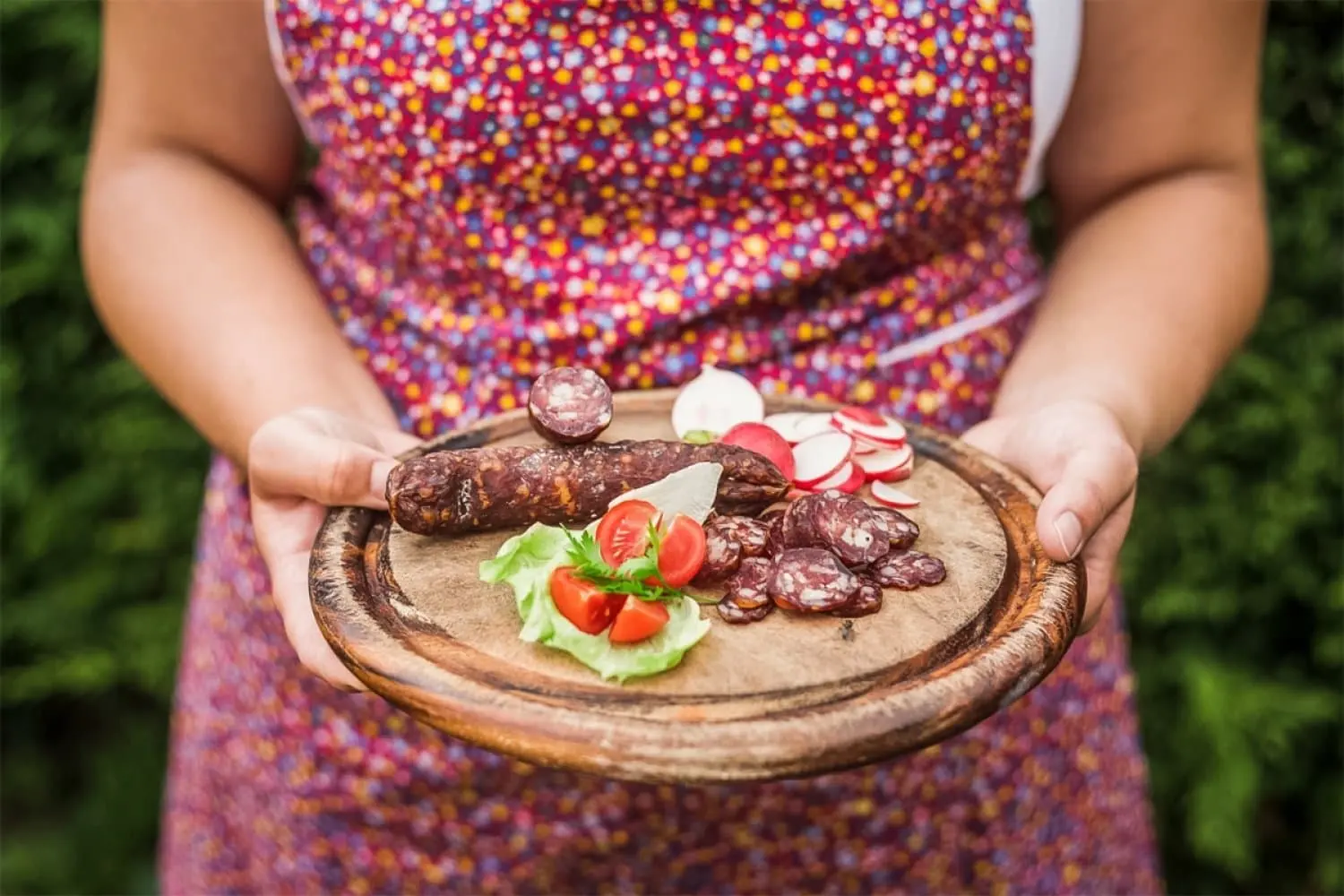 Bäuerin hält ein Holzbrett mit Kaminwurzen, Radieschen und Tomaten