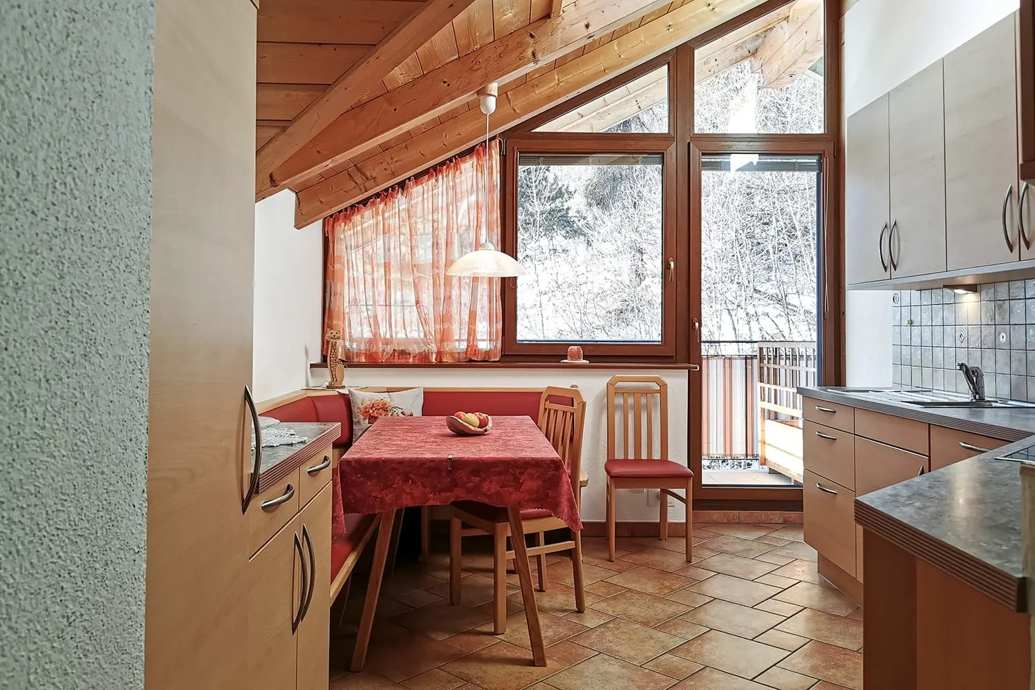 Wohnküche mit Essecke und rot karierter Tischdecke unter der Holzdecke